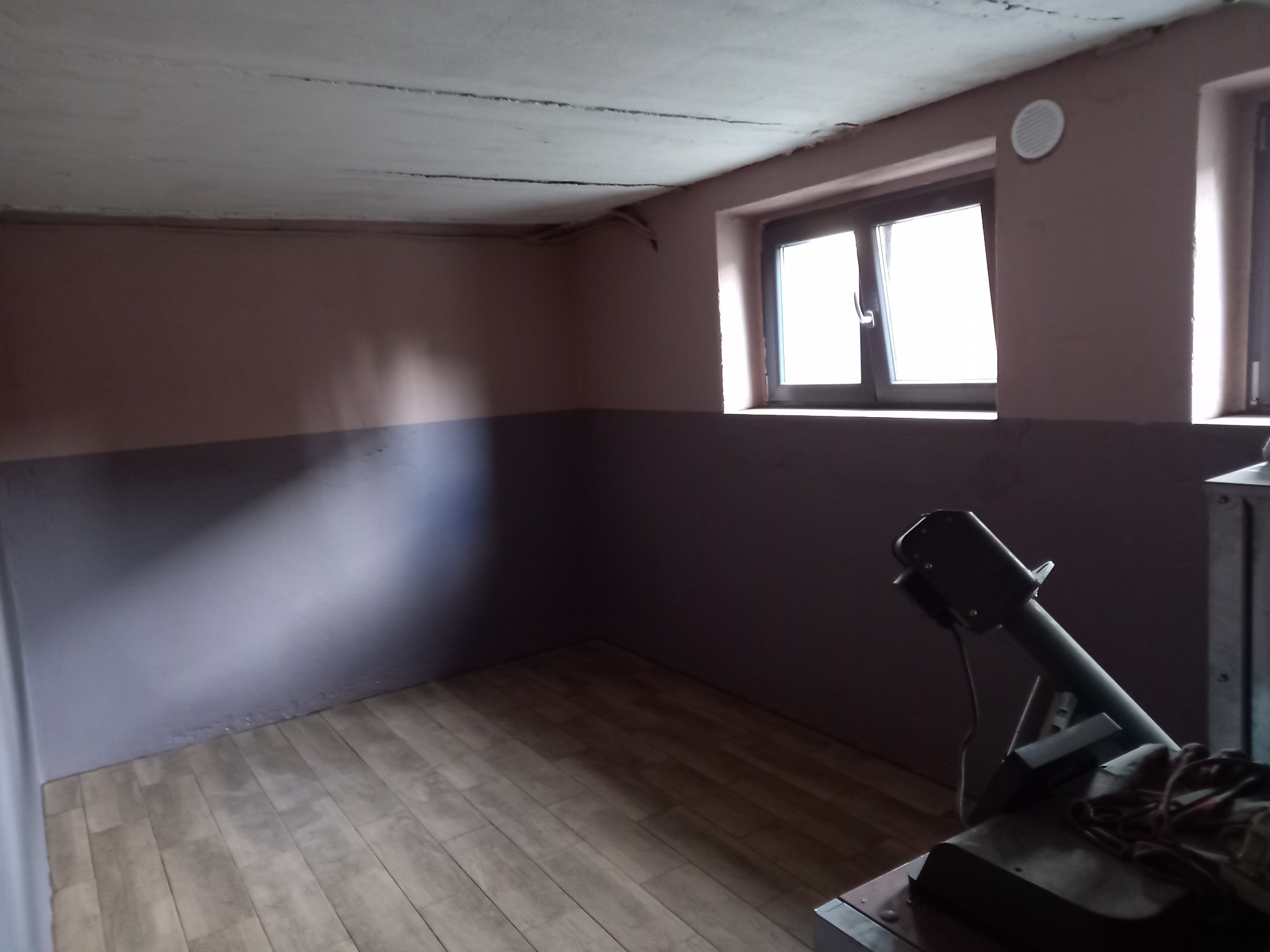 Pomieszczenie po malowaniu ścian na dwa kolory, z widocznym sprzętem malarskim, drewnopodobną podłogą i oknami.