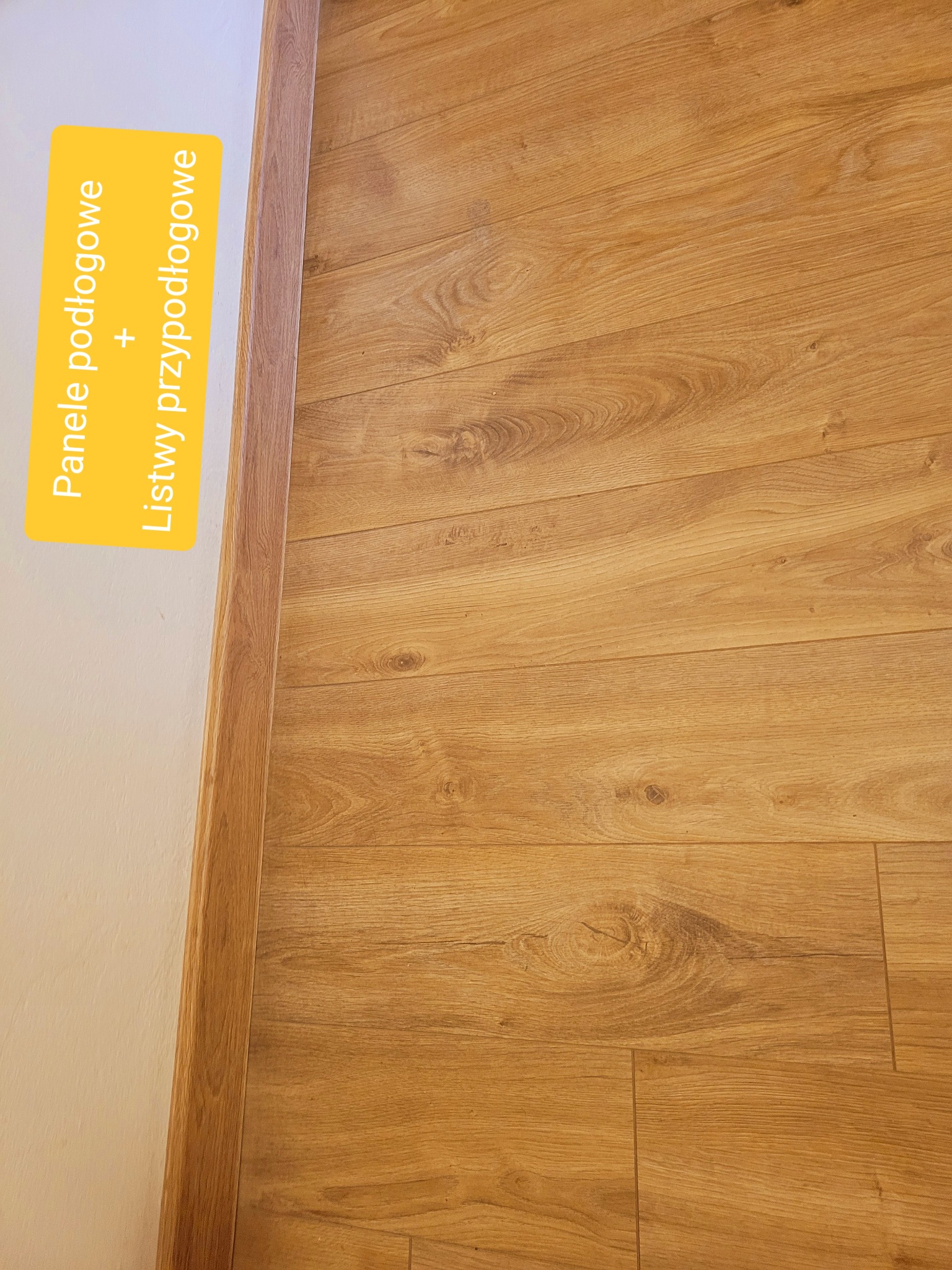 Ułożone panele podłogowe w odcieniach dębu z dopasowanymi listwami przypodłogowymi, widoczne łączenia paneli i delikatna faktura drewna.