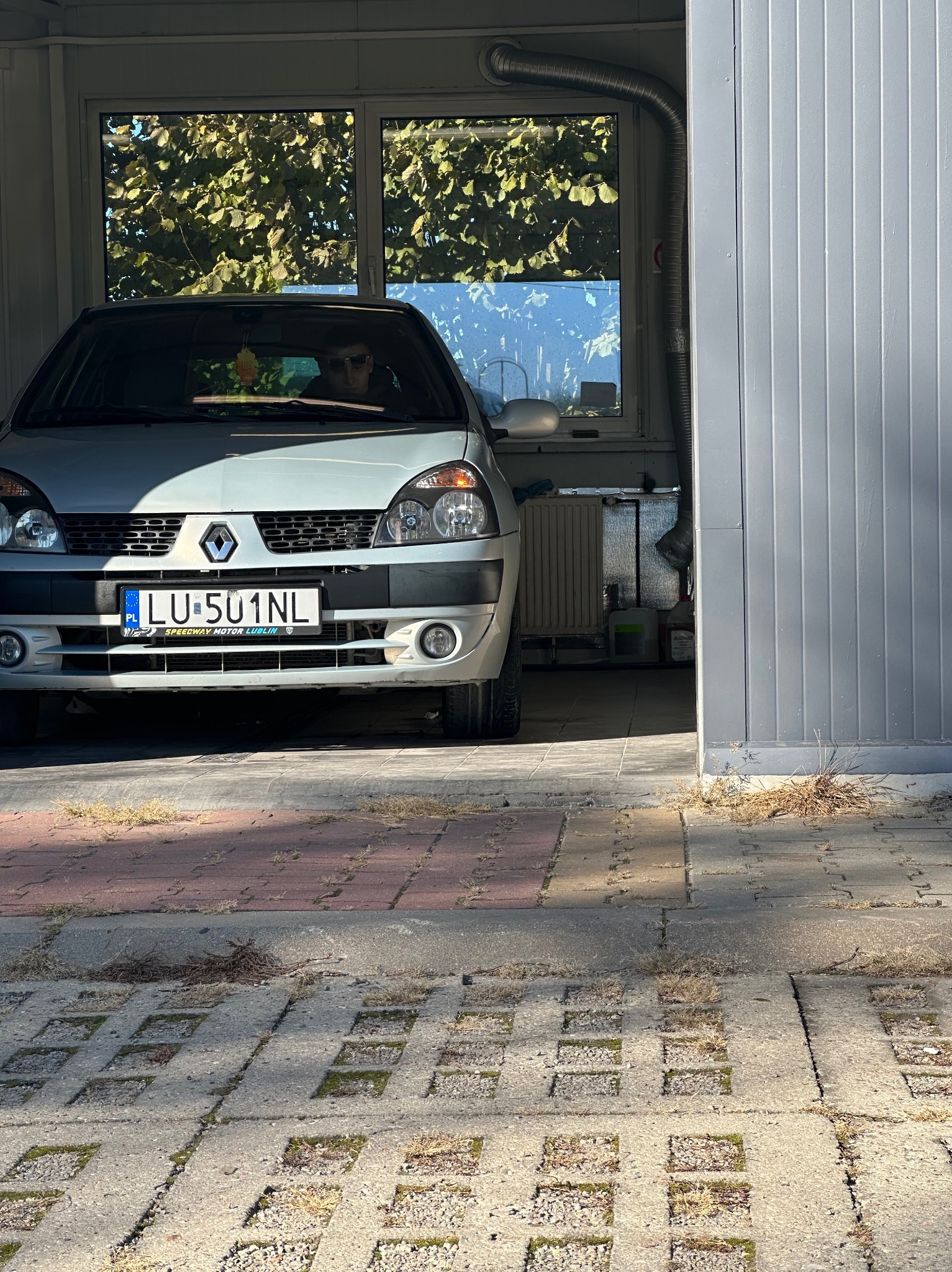 Srebrny Renault Clio z lubelską rejestracją LU 501NL zaparkowany w garażu, widoczny kierowca w okularach za kierownicą, na ścianie garażu widać instalację wentylacyjną.