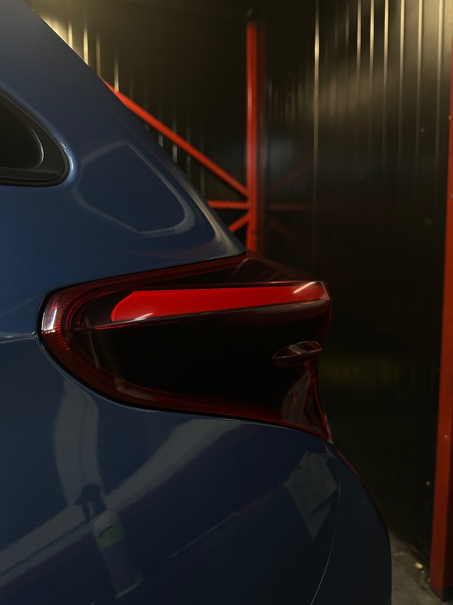 Błyszczący, niebieski lakier na tylnej części samochodu, z widocznym światłem stopu i elementami konstrukcji w tle.