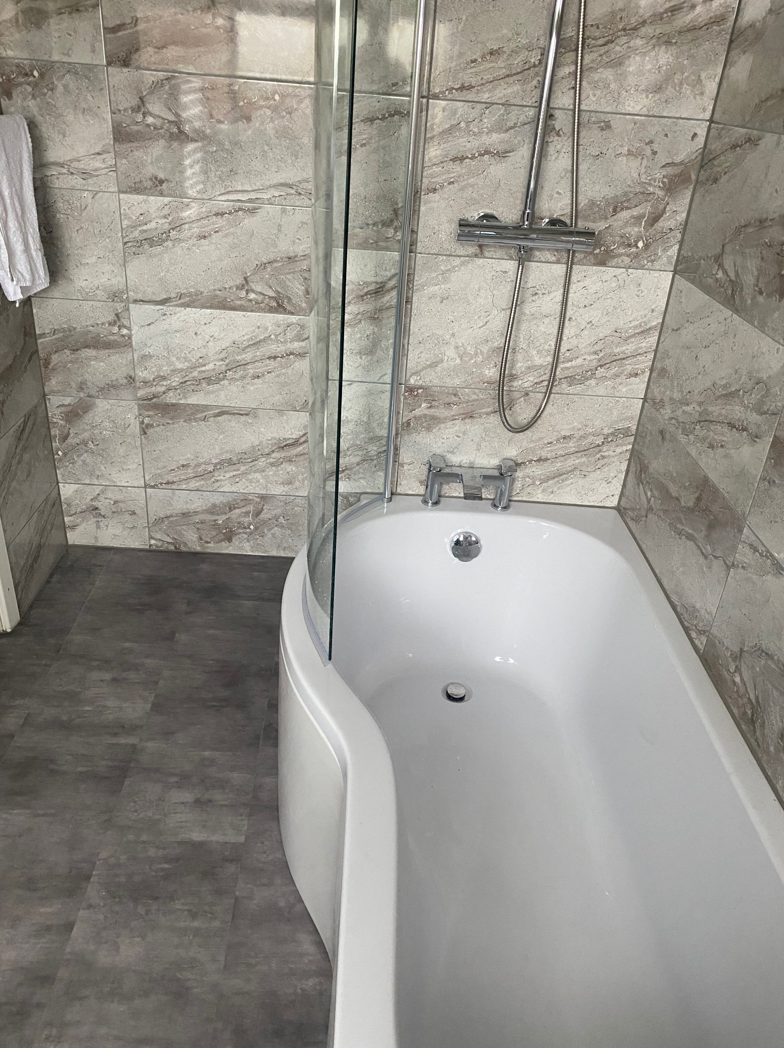 Nowoczesna łazienka z wanną z parawanem nawannowym, wykończona płytkami imitującymi marmur na ścianach i szarą podłogą.