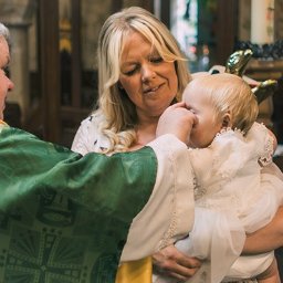 ZoomArt - Ksiądz w zielonej szacie udziela sakramentu chrztu płaczącemu niemowlęciu w białej sukience, trzymanemu przez matkę w kościele.