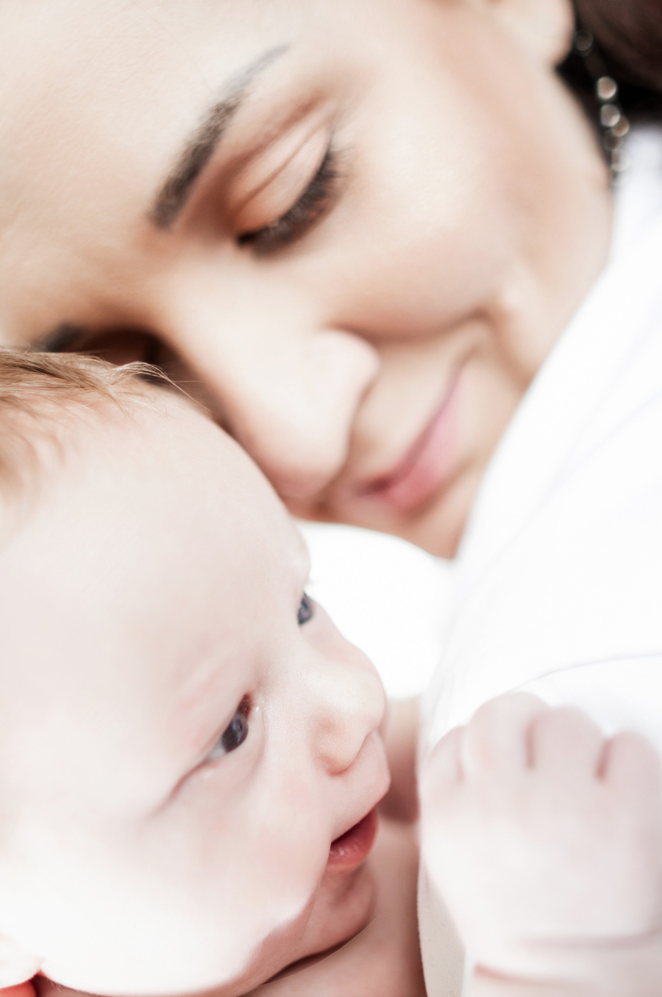 Delikatne ujęcie matki spoglądającej z czułością na swoje niemowlę, z wyraźnym skupieniem na ich twarzach i subtelnym oświetleniu.