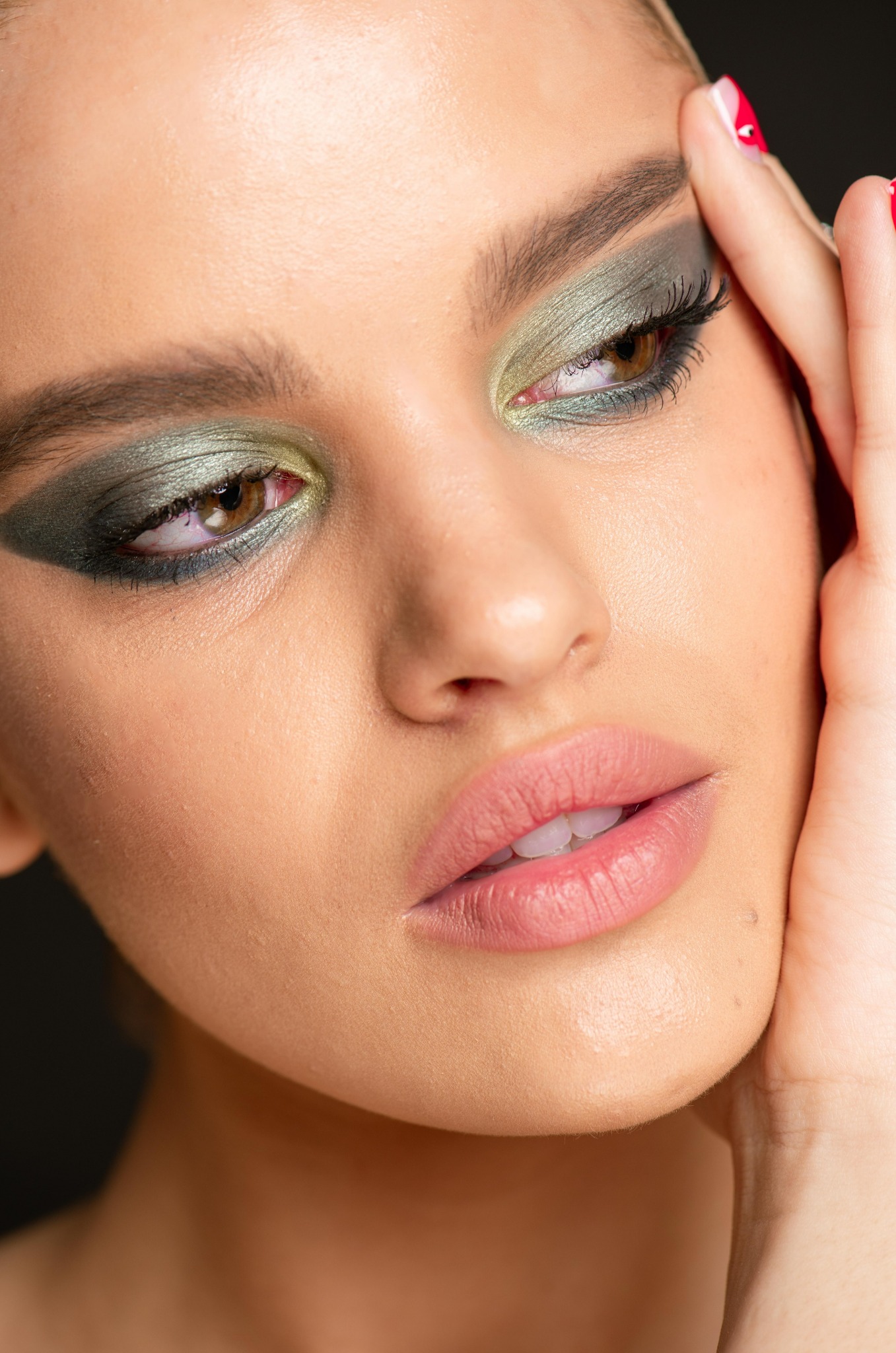 Portret kobiety z intensywnym makijażem oczu w odcieniach zieleni i brązu, dłoń delikatnie dotyka skroni, podkreślając wyrazistość spojrzenia.