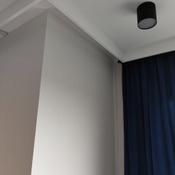 Przemysław Paziuk Front Home - Pomalowany narożnik pokoju z eleganckim sufitem podwieszanym, oświetleniem punktowym i granatowymi zasłonami.