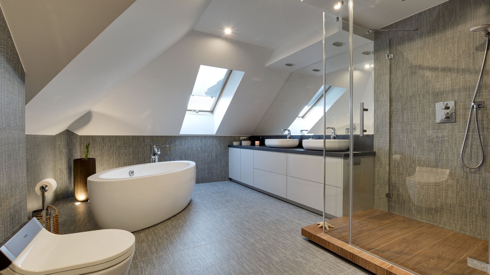 Nowoczesna łazienka na poddaszu ze skośnym sufitem i oknami dachowymi, wyposażona w wolnostojącą wannę, kabinę prysznicową ze szklaną ścianą i drewnianym brodzikiem, oraz umywalkę nablatową...