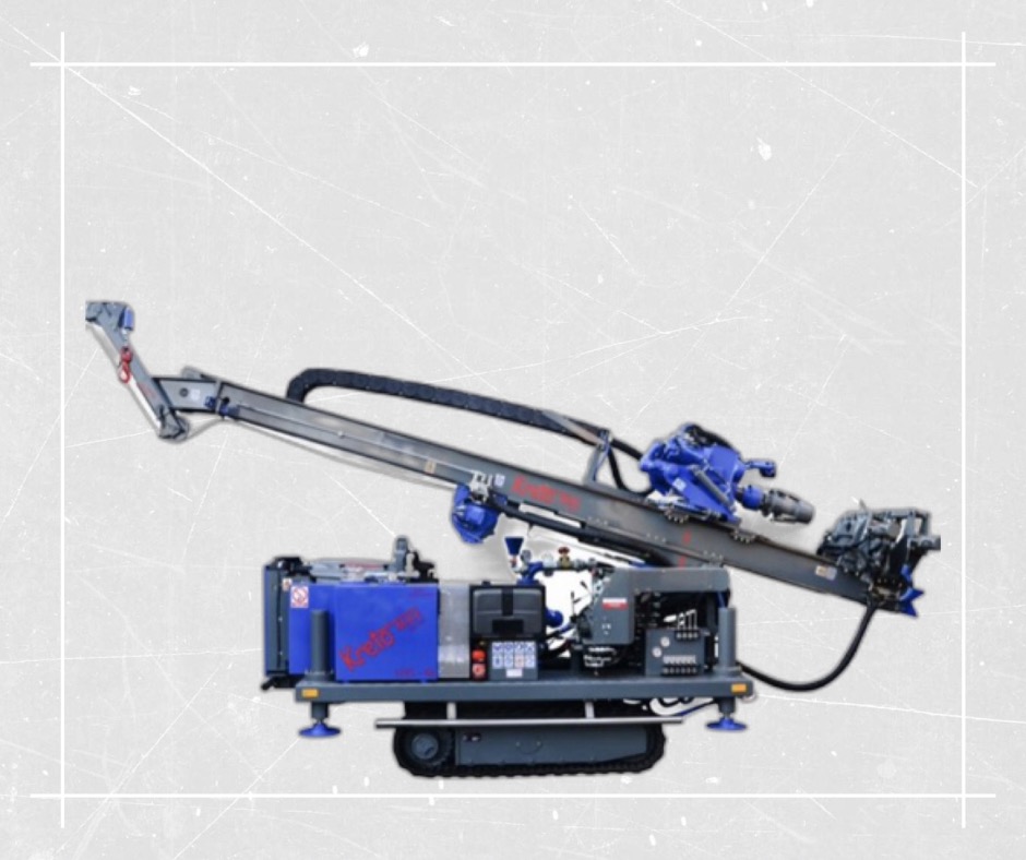 Mobilna wiertnica geotermalna z wysięgnikiem, niebieskimi elementami i logotypem na obudowie, na tle szarej, teksturowanej powierzchni.