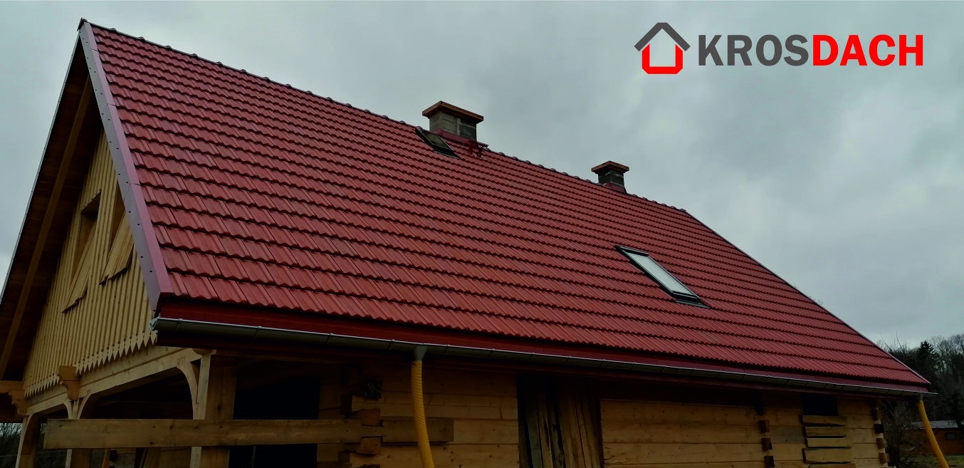 Czerwony dach z blachodachówki z oknem dachowym i kominami na drewnianym domu w stylu góralskim, widoczne orynnowanie i logo firmy na górze zdjęcia.