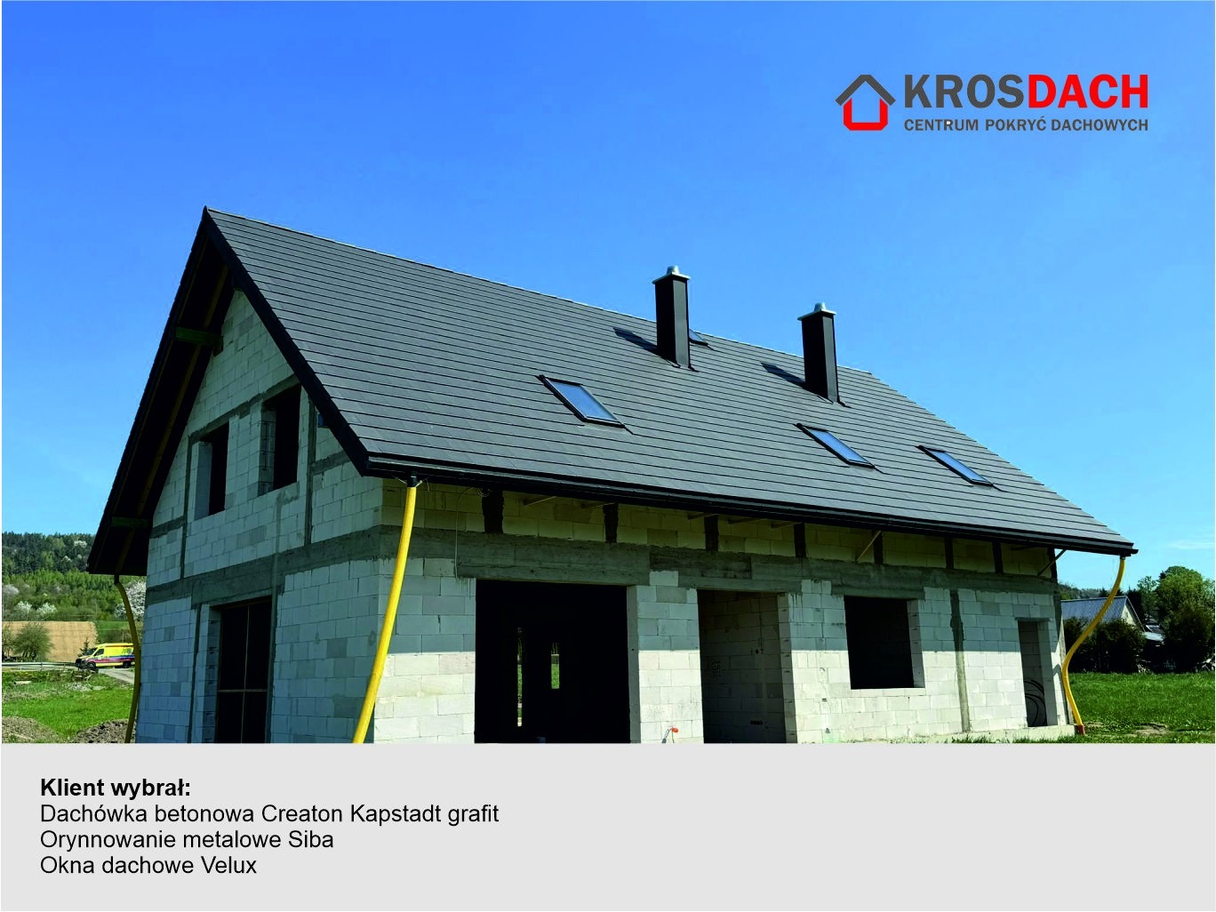 Dom w trakcie budowy z grafitową dachówką betonową Creaton Kapstadt, metalowym systemem orynnowania Siba i oknami dachowymi Velux, widoczne kominy i fragment krajobrazu.