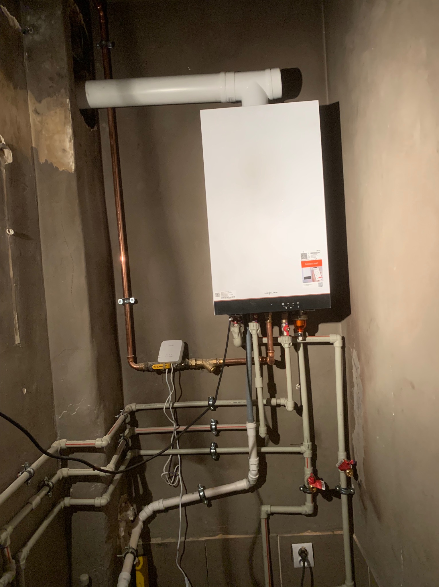 Nowy, biały piec gazowy Viessmann zamontowany na ścianie z widocznymi rurami miedzianymi i plastikowymi, oraz fragmentem instalacji odprowadzającej spaliny.