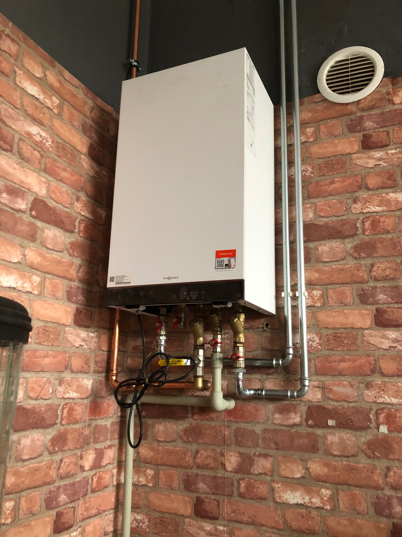 Biały piec gazowy Viessmann zamontowany na ścianie z czerwonej cegły, widoczne rury miedziane i stalowe, oraz fragment instalacji.