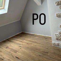 NATALIIA DEMCHUK - Poddasze po remoncie: nowa podłoga z paneli drewnopodobnych, ściany pomalowane na szaro, dekoracyjna ściana z białej cegły, okno dachowe wpuszczające światło.