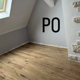 Poddasze po remoncie: nowa podłoga z paneli drewnopodobnych, ściany pomalowane na szaro, dekoracyjna ściana z białej cegły, okno dachowe wpuszczające światło.