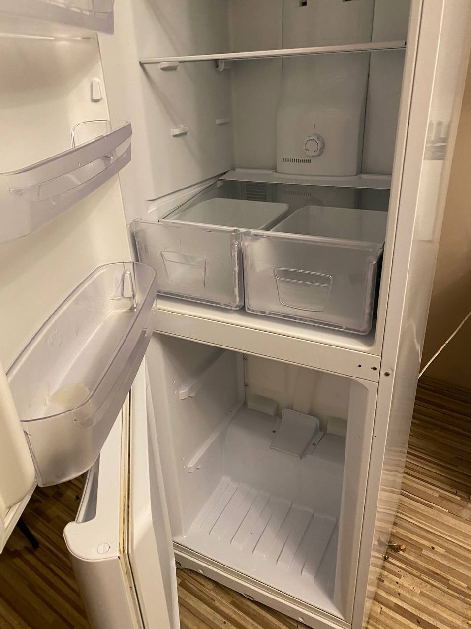 Wnętrze czystej, otwartej lodówki z przezroczystymi szufladami i półkami, widoczna regulacja temperatury.