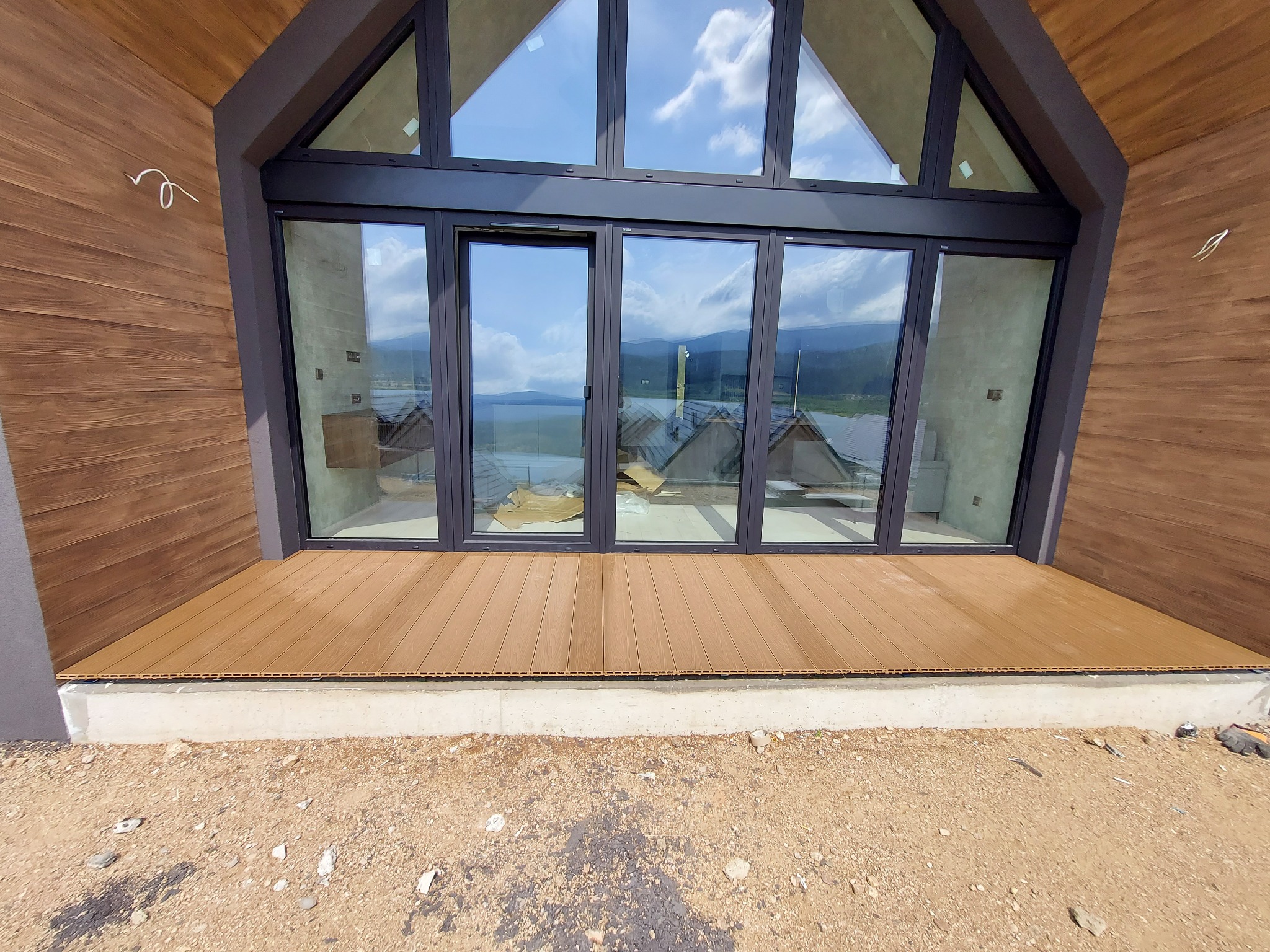 Nowoczesny taras z desek kompozytowych, widok z zewnątrz, z dużymi przesuwnymi drzwiami i widokiem na góry w tle.