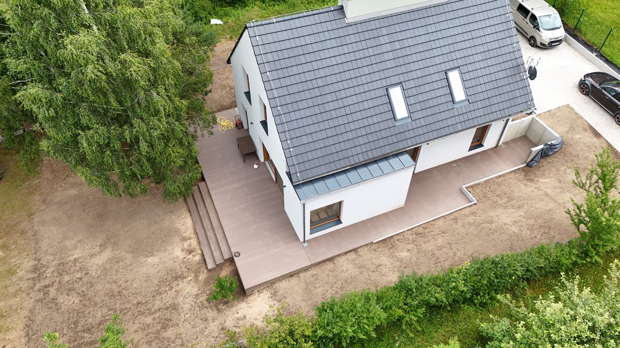 Nowoczesny dom jednorodzinny z szarą dachówką i tarasem z kompozytu w kolorze drewna, widok z góry.