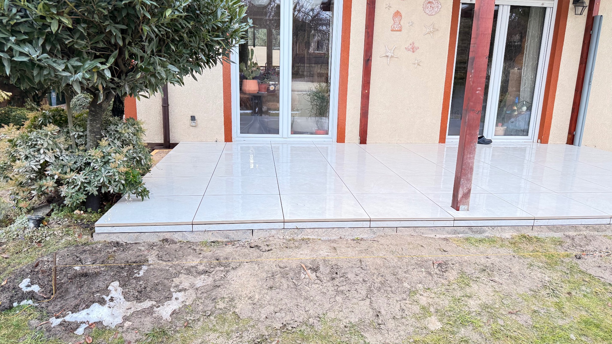 Jasne, ceramiczne płytki tarasowe ułożone we Wrocławiu, z widocznym fragmentem ogrodu i elementami konstrukcyjnymi budynku. Minimalistyczny design.