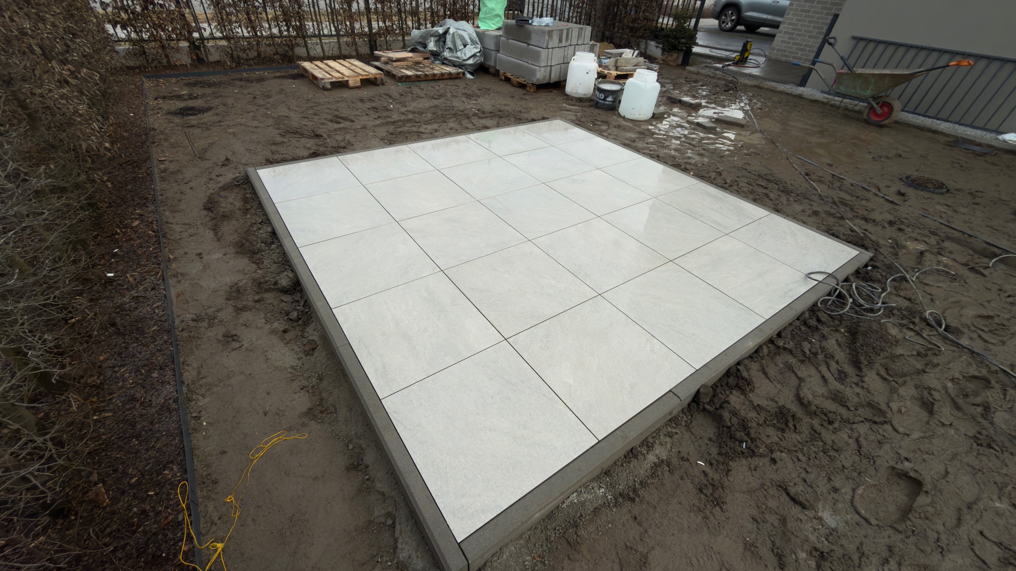 Układanie jasnych płyt na tarasie we Wrocławiu. Widoczne narzędzia i materiały budowlane. Prace w toku, teren przygotowany pod dalsze etapy.