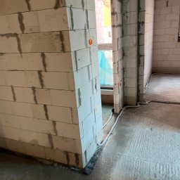 ENGETIA - Surowy stan wnętrza budynku w trakcie budowy, widoczne ściany z betonu komórkowego, okno z niebieską folią ochronną i wystające przewody elektryczne.