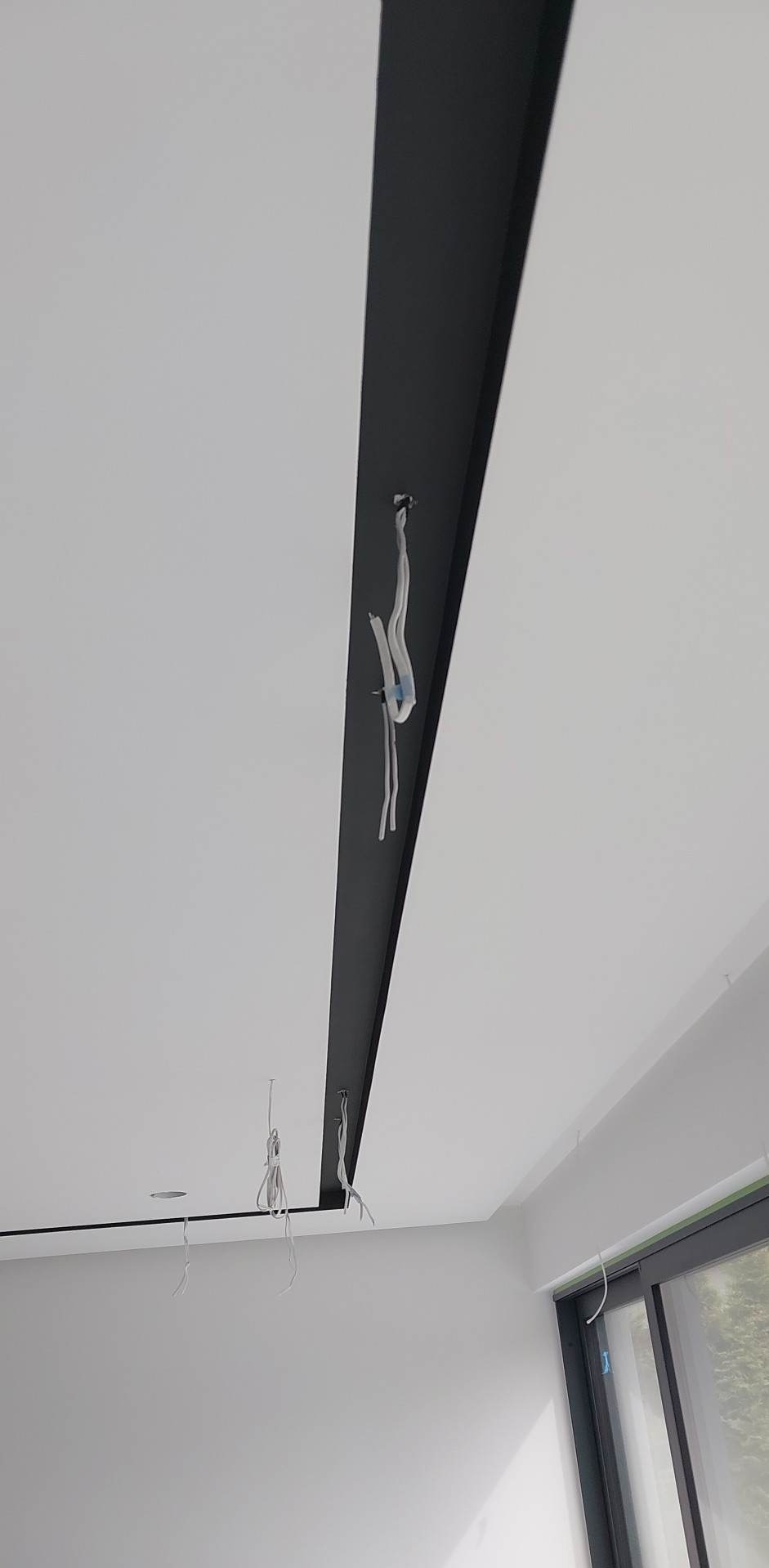 Biały sufit z czarnym, wpuszczonym pasem, z którego wystają kable elektryczne przygotowane do montażu oświetlenia.