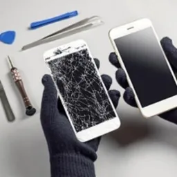 Dłonie w czarnych rękawiczkach trzymają dwa telefony: jeden z pękniętym ekranem, drugi z czystym ekranem. Obok leżą narzędzia do naprawy, w tym śrubokręty i pincety.