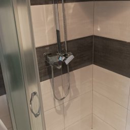 PROMONI Monika Pilarska - Kabina prysznicowa z chromowaną armaturą na tle płytek w odcieniach beżu i brązu, widoczna także pralka Inex.