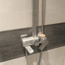 Zakamieniona bateria prysznicowa z mydłem na wierzchu, na tle białych i szarych płytek.