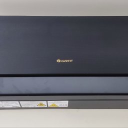 VENTUS - KLIMA Rafał Kućmierz - Czarna jednostka wewnętrzna klimatyzacji marki Gree, widoczna od frontu na jasnym tle, z naklejkami ostrzegawczymi w dolnej części obudowy.