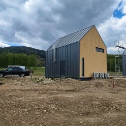 VENTUS - KLIMA Rafał Kućmierz - Nowoczesne domki modułowe z pompami ciepła AUX na zewnątrz, teren w trakcie zagospodarowania, w tle zalesione wzgórza i firmowy samochód.