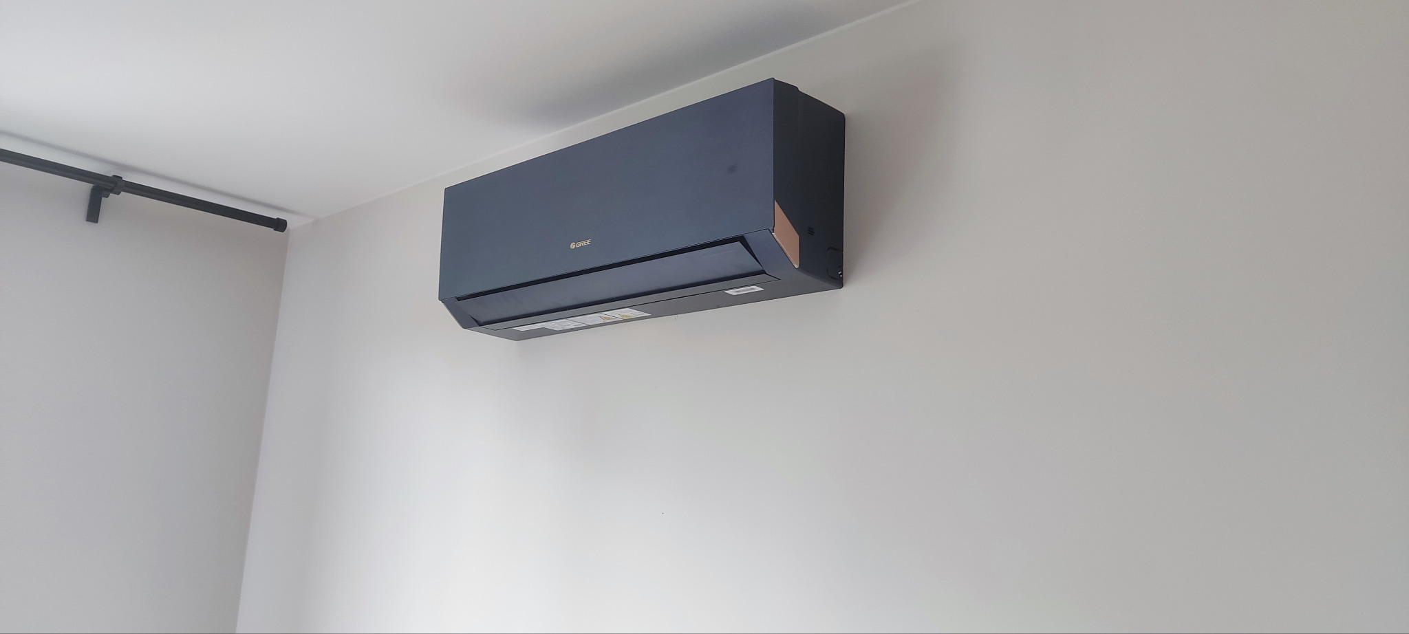 Czarny klimatyzator marki Gree zamontowany na jasnej ścianie, widoczny fragment karnisza.