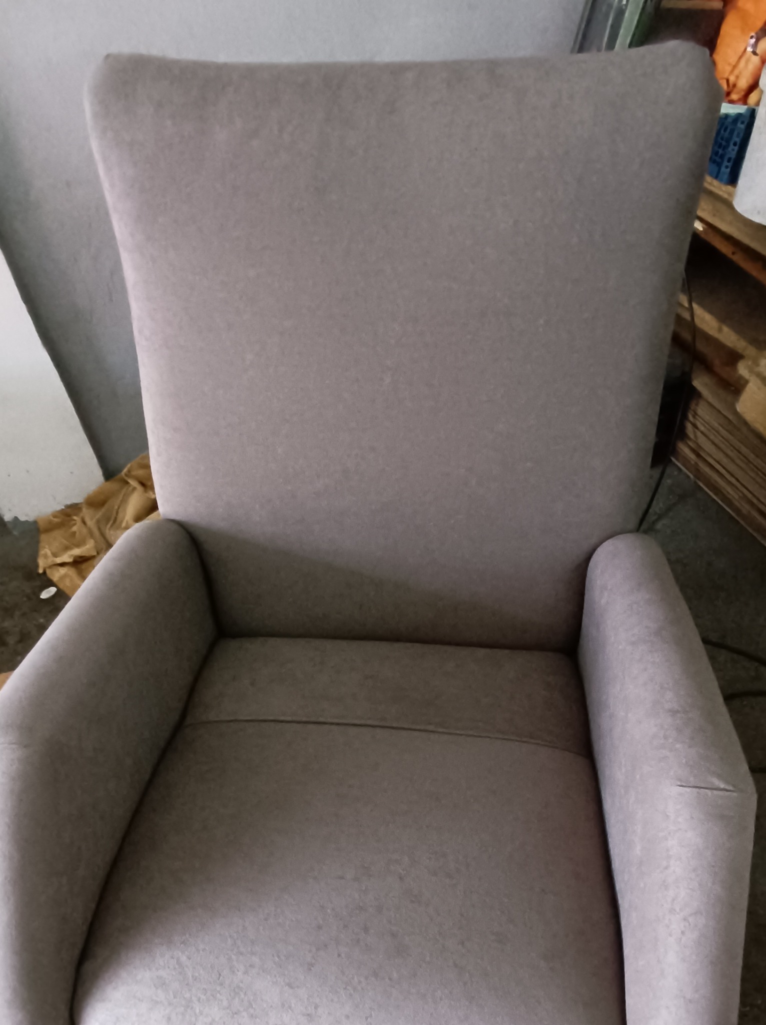 Beżowy fotel tapicerowany z wysokim oparciem, widok z przodu, na tle ściany i elementów drewnianych.