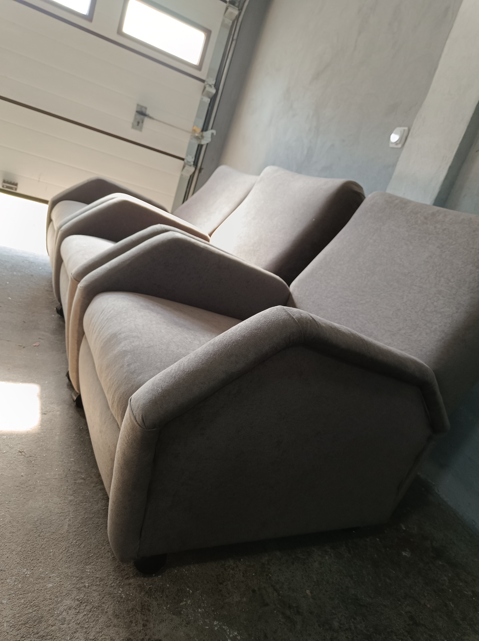 Rząd beżowych, tapicerowanych foteli z wysokimi oparciami, ustawionych w garażu na betonowej podłodze, widok z boku i dołu, z otwartą bramą garażową w tle.