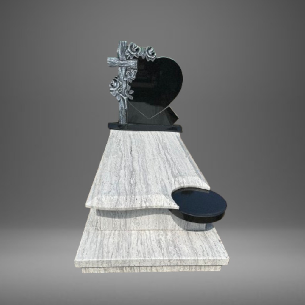 Wielopoziomowy pomnik z jasnego, żyłkowanego kamienia, zwieńczony czarnym sercem i krzyżem z motywem róż, z okrągłym, czarnym wgłębieniem na kwiaty.