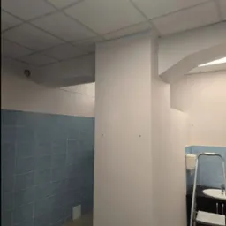 Świeżo pomalowane na biało ściany w pomieszczeniu z niebieskimi płytkami, widoczna drabina aluminiowa i fragment umywalki, sufit kasetonowy z oświetleniem.