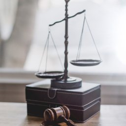 Kancelaria Prawna TEBI. Prawo gospodarcze, prawo pracy - tebi.com.pl - Waga sprawiedliwości i drewniany młotek sędziowski na skórzanym pudełku, neutralne tło.