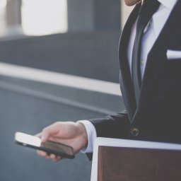 Kancelaria Prawna TEBI. Prawo gospodarcze, prawo pracy - tebi.com.pl - Mężczyzna w garniturze przegląda coś na smartfonie, trzymając w ręku skórzany notatnik.