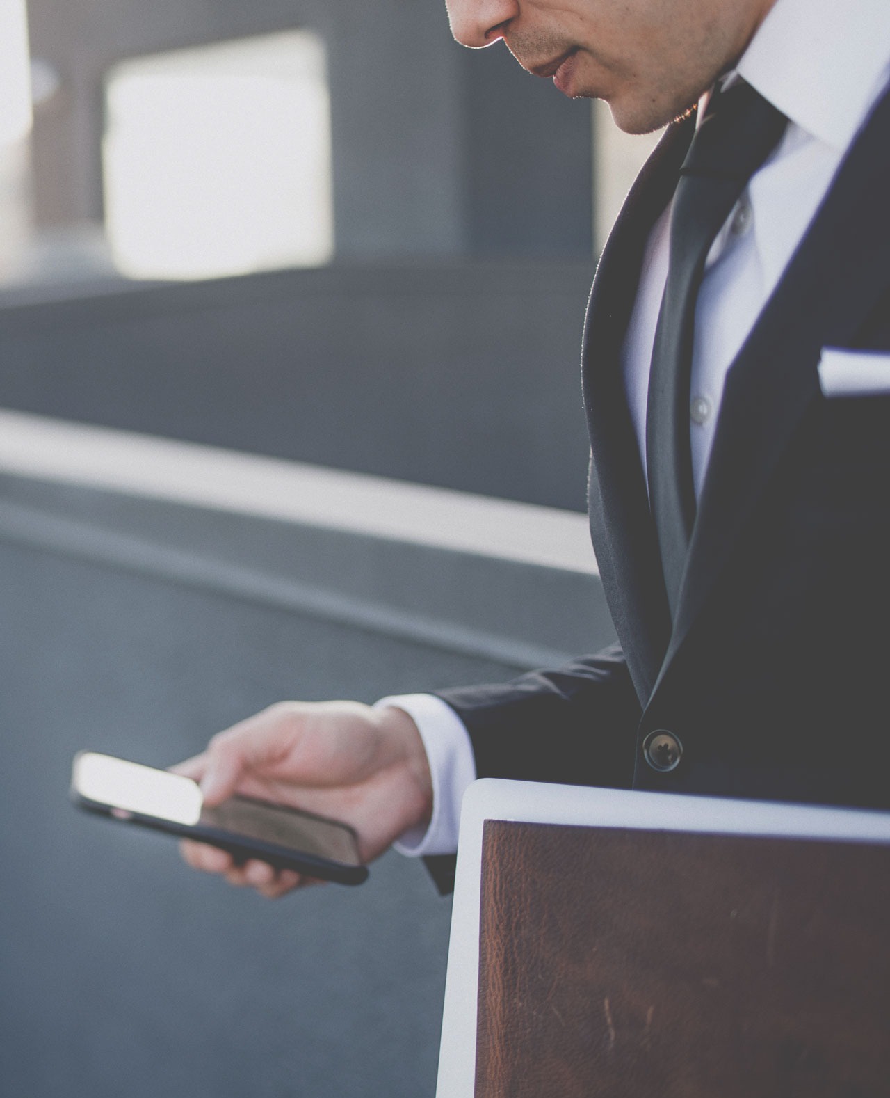 Mężczyzna w garniturze przegląda coś na smartfonie, trzymając w ręku skórzany notatnik.