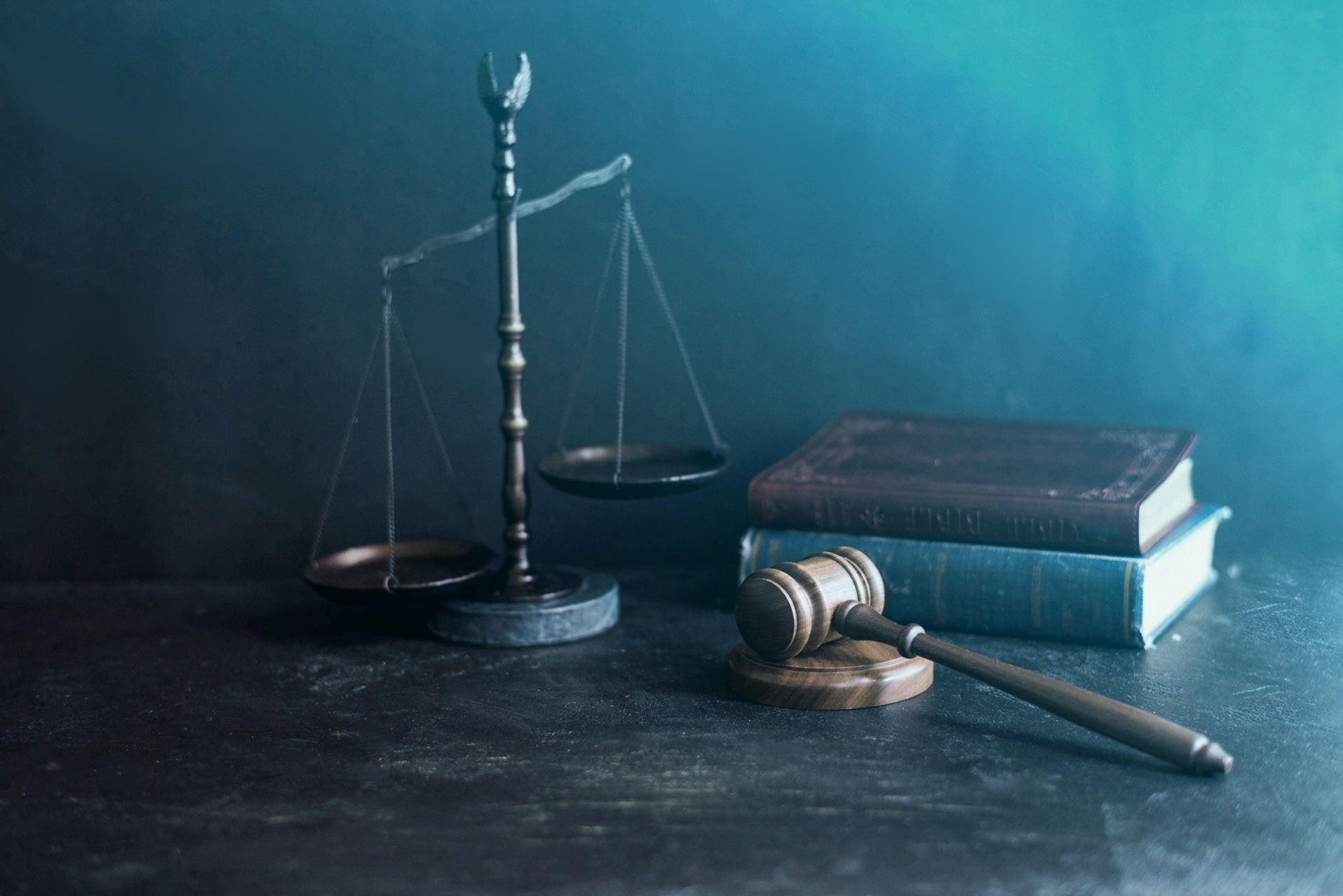 Waga sprawiedliwości, drewniany młotek i dwa tomy książek na ciemnym, teksturowanym tle z subtelnym niebieskim oświetleniem.