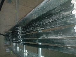 Rząd czarnych rur instalacyjnych prowadzonych równolegle na metalowej konstrukcji wsporczej w Śremie. Widoczne mocowania i elementy złączne, całość w surowym, industrialnym otoczeniu.