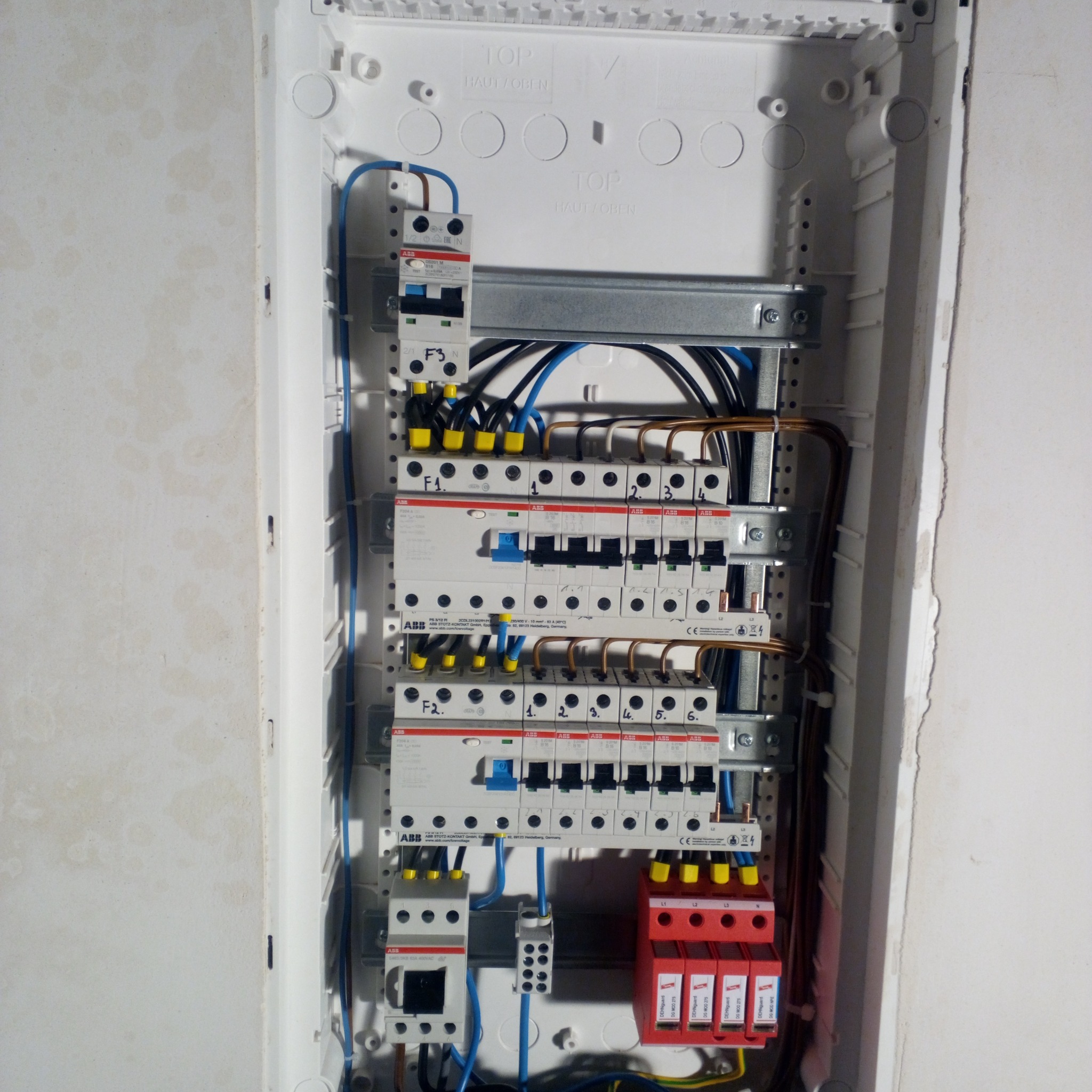 Rozdzielnica elektryczna ABB z zamontowanymi bezpiecznikami i ogranicznikami przepięć DEHNguard, widoczne kable w kolorach niebieskim, czarnym i brązowym, żółte końcówki kablowe, zamocowana...