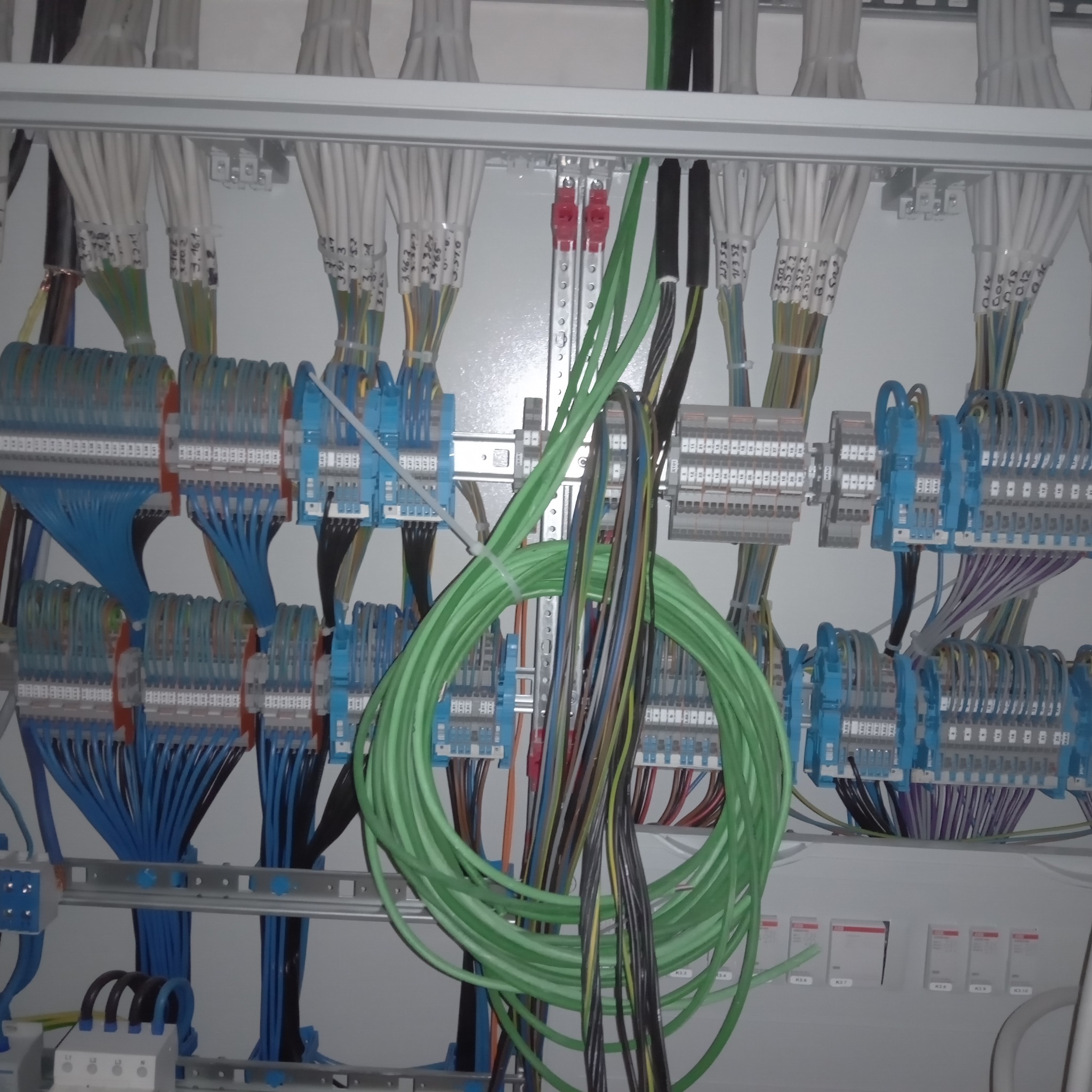 Rozdzielnica elektryczna z uporządkowanymi przewodami o różnych kolorach, podłączonymi do listew zaciskowych. Przewody opisane etykietami.