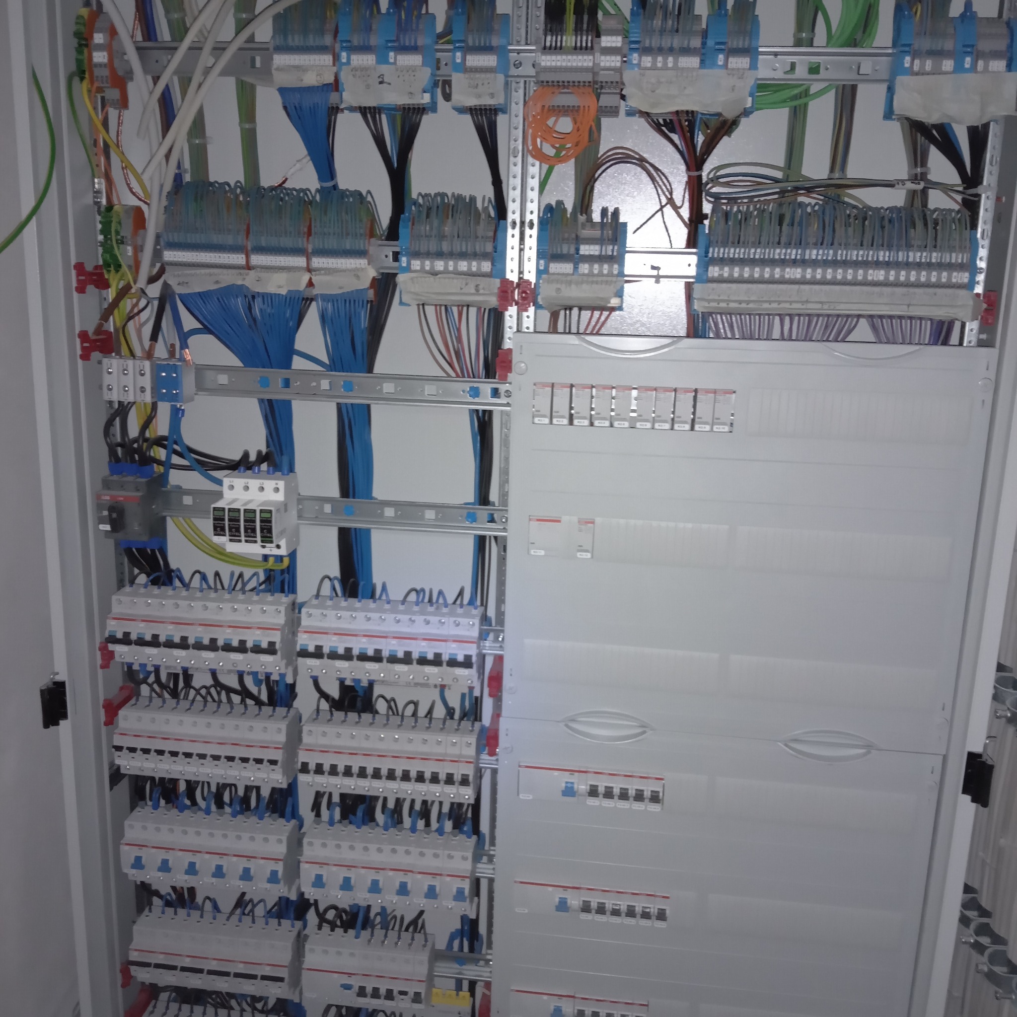 Rozdzielnica elektryczna z licznymi bezpiecznikami, przewodami w różnych kolorach i listwami zaciskowymi, widoczne elementy automatyki i zabezpieczeń.