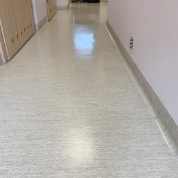 AMD Magnolia BIS - Błyszcząca, jasna podłoga korytarza w budynku biurowym, widoczne drzwi po lewej stronie i wentylacja w ścianie po prawej.