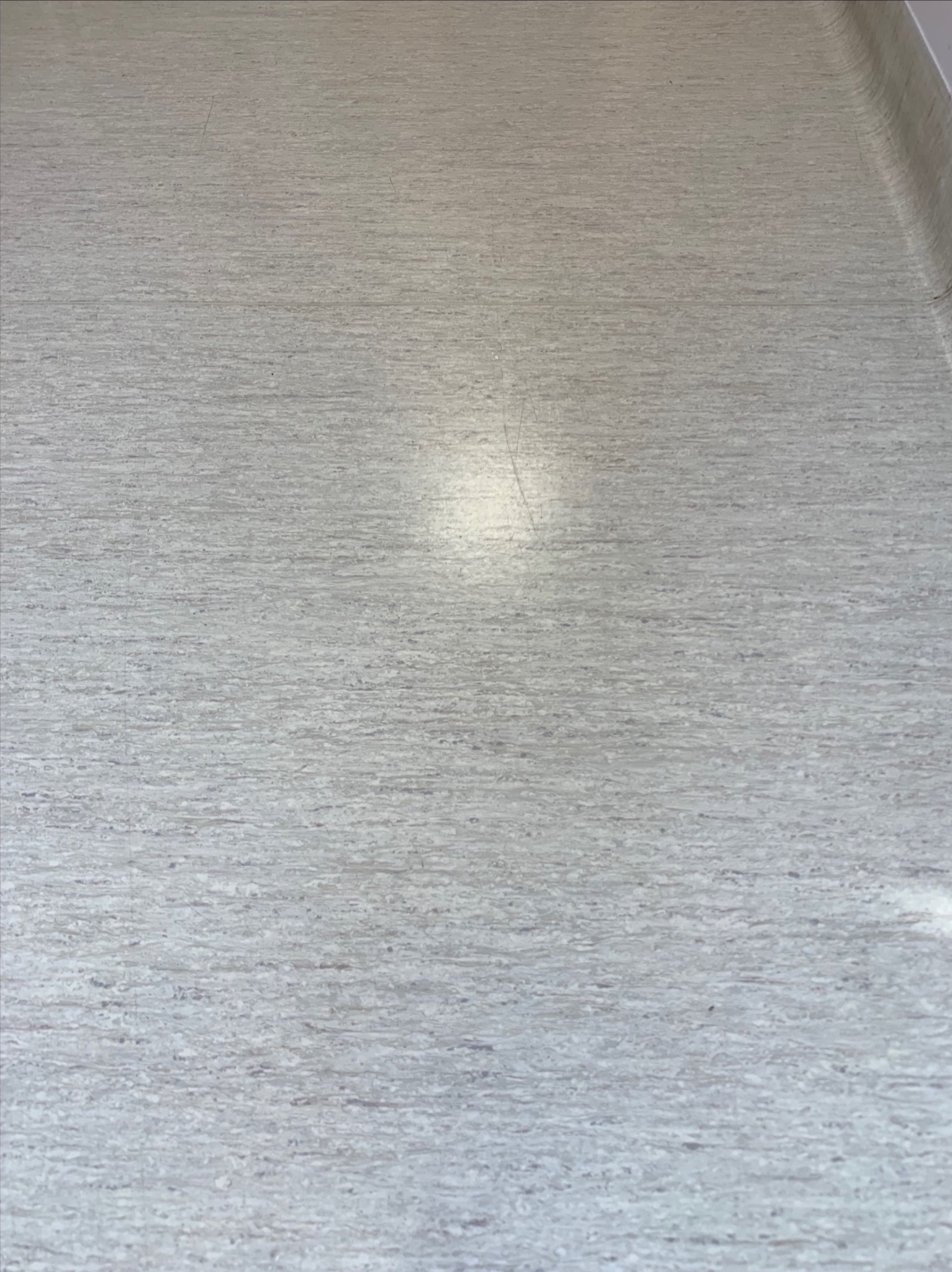 Jasnoszara, wzorzysta podłoga z linoleum, widoczne drobne zarysowania i refleksy świetlne.