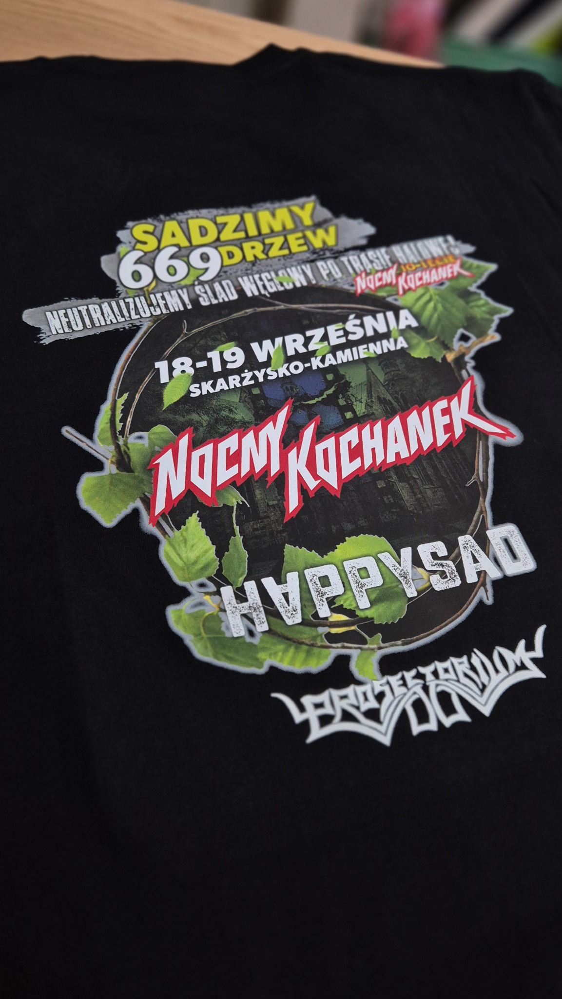 Czarna koszulka z nadrukiem grafiki zespołu 'Nocny Kochanek', informującym o sadzeniu drzew 18-19 września w Skarżysku-Kamiennej. Wyraźne detale nadruku.