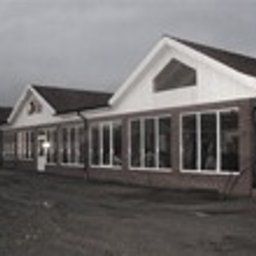 P.P.H.U. ERA-SZKŁO - Długi budynek z szeregiem dużych okien, widok z zewnątrz w pochmurny dzień, brak wyraźnych detali architektonicznych.