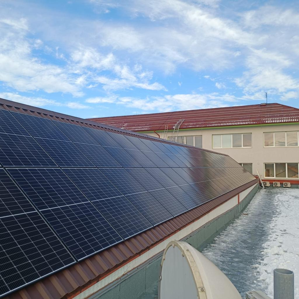Instalacja paneli słonecznych na dachu budynku przemysłowego z widoczną anteną satelitarną i błękitnym niebem
