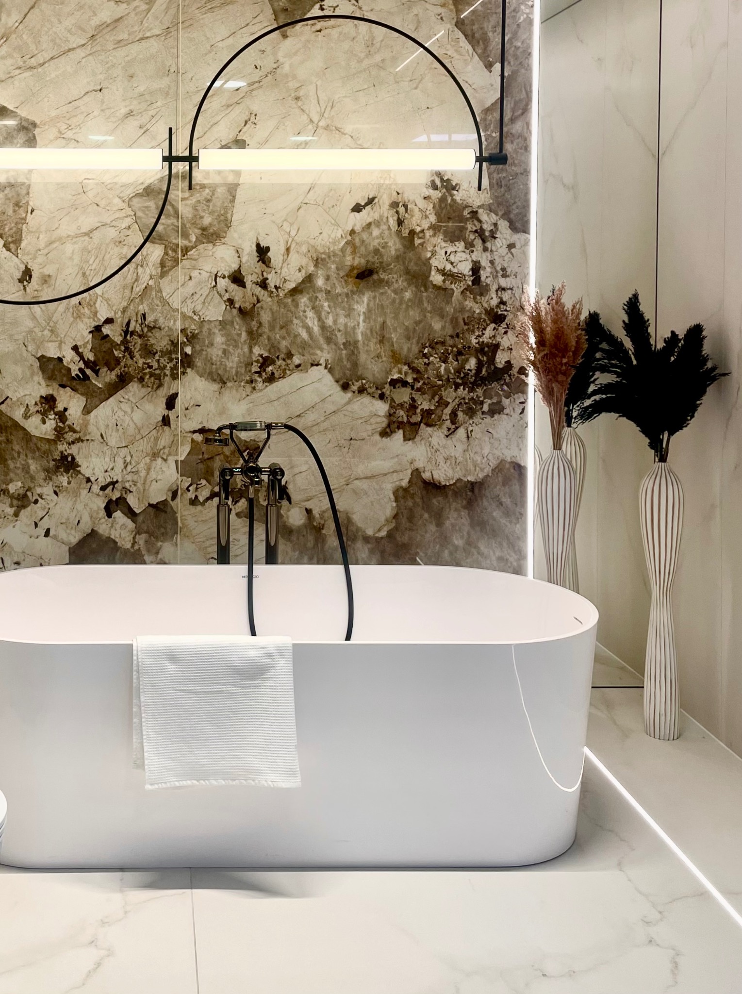 Elegancka łazienka z wolnostojącą wanną, chromowaną armaturą i dekoracyjną ścianą z marmuru, oświetlona nowoczesną lampą i akcentującymi listwami led.