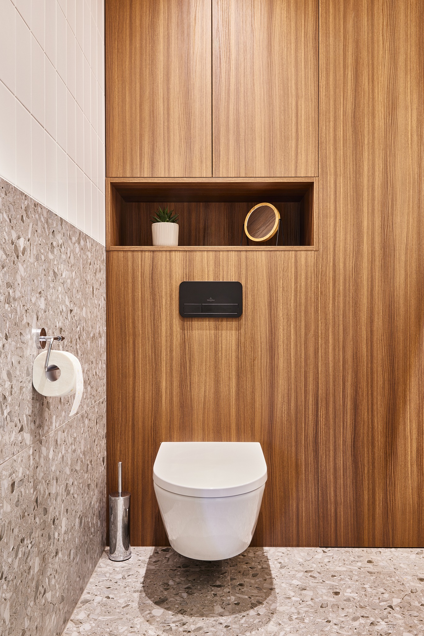 Nowoczesna łazienka: podwieszana toaleta Villeroy&Boch na tle drewnianej zabudowy z półką, na której stoi roślina i lusterko. Płytki lastryko na podłodze i ścianie.