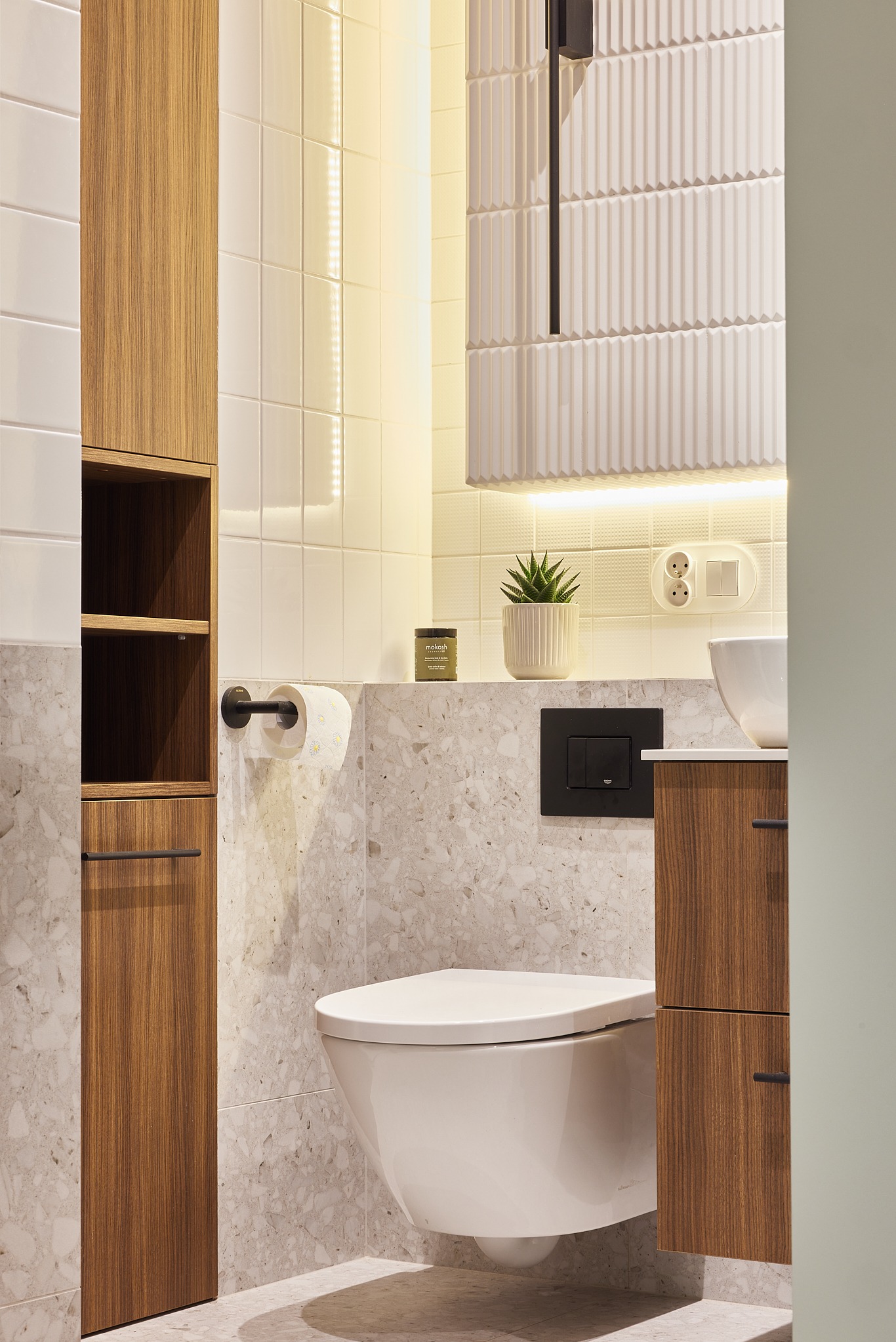 Nowoczesna łazienka z wiszącą toaletą, szafkami z forniru orzechowego i mozaiką lastryko. Podświetlane lustro i półki dodają elegancji.
